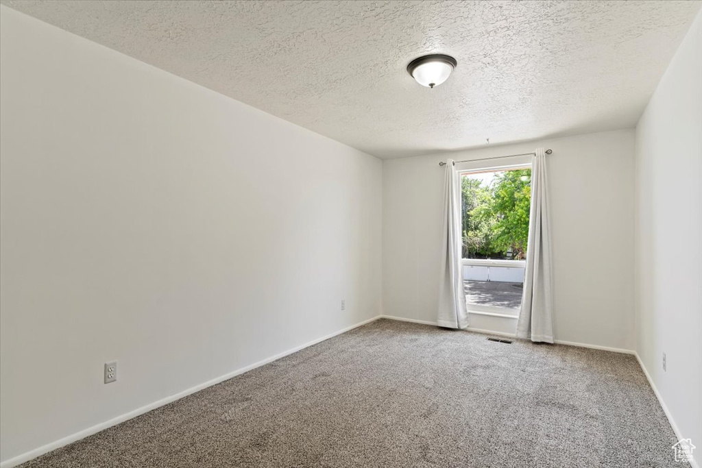 Carpeted empty room with a textured ceiling and baseboards