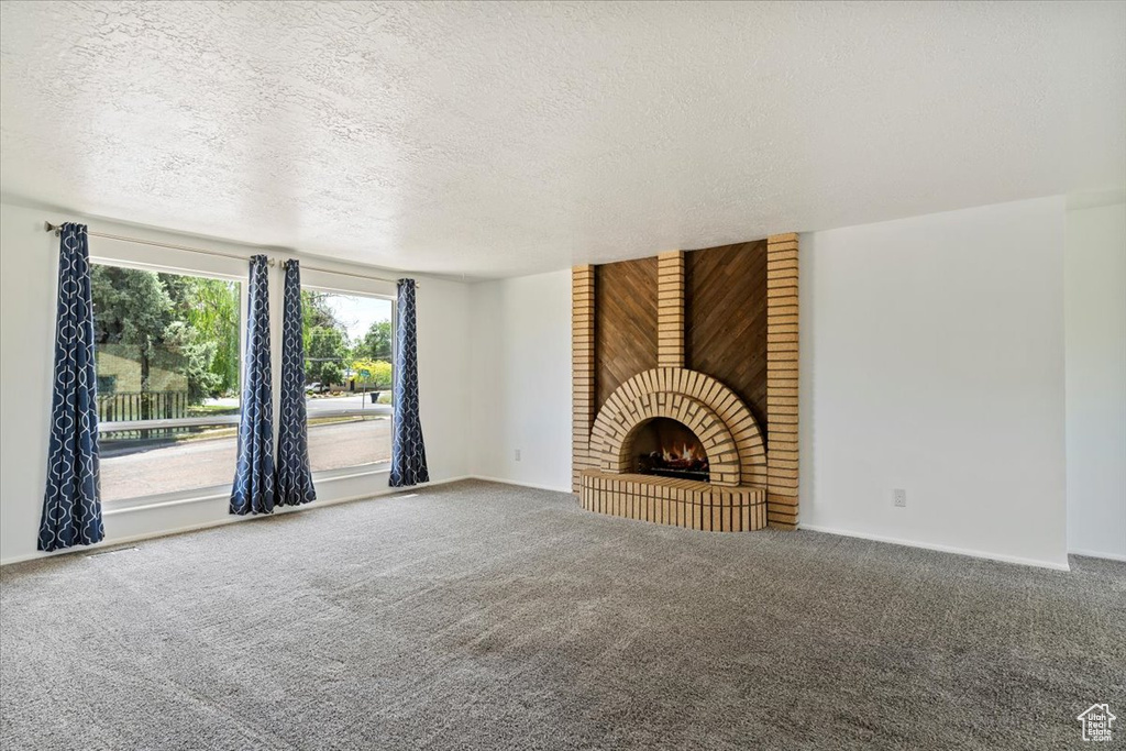 Unfurnished living room with carpet flooring, a textured ceiling, and a brick fireplace