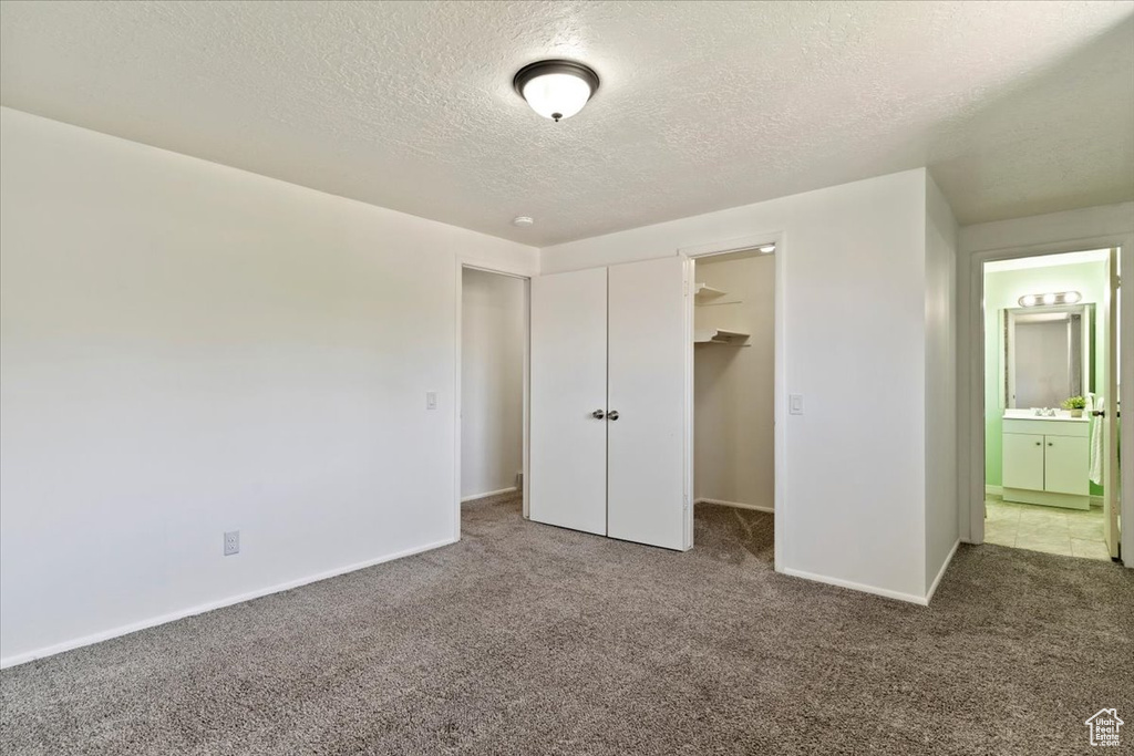 Unfurnished bedroom featuring carpet, a textured ceiling, a spacious closet, a closet, and connected bathroom