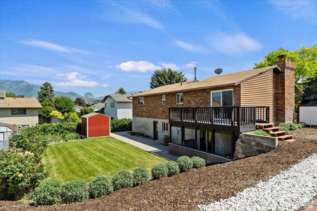 Back of property with a storage unit, a deck with mountain view, a yard, a patio area, and a chimney