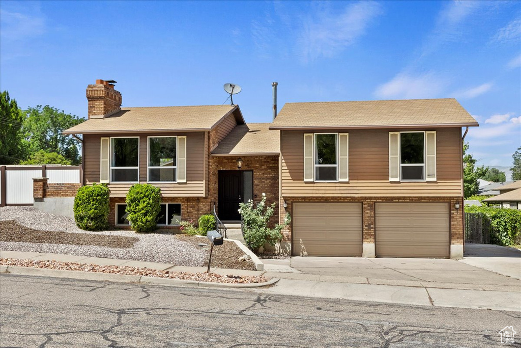 Bi-level home featuring a chimney, an attached garage, concrete driveway, and brick siding