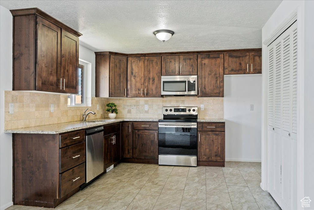 Kitchen featuring appliances with stainless steel finishes, backsplash, dark brown cabinetry, and a textured ceiling