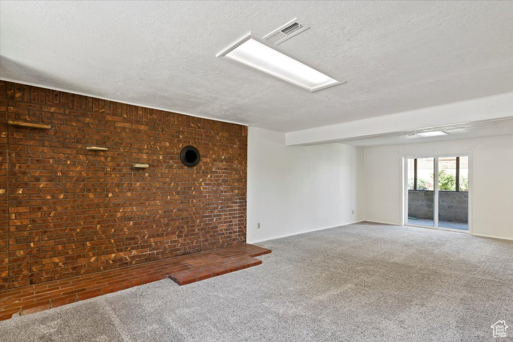 Unfurnished room with a textured ceiling, carpet, and brick wall