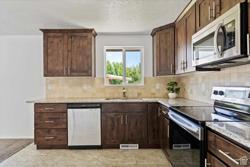 Kitchen with stainless steel appliances, light stone counters, a textured ceiling, decorative backsplash, and dark brown cabinets