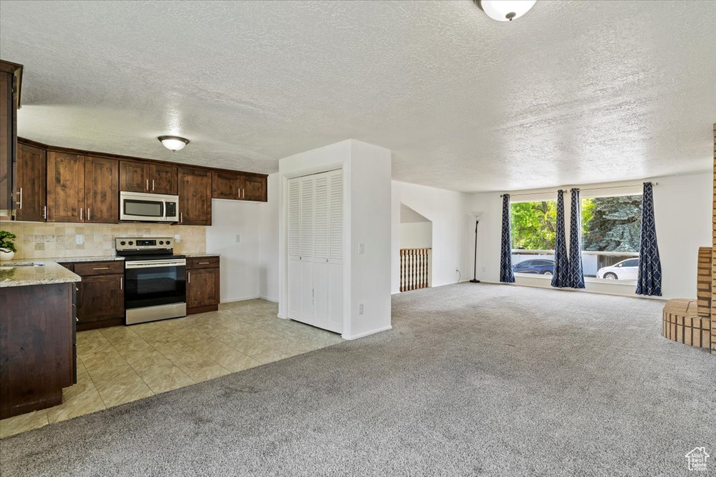 Kitchen featuring appliances with stainless steel finishes, light carpet, dark brown cabinets, open floor plan, and a textured ceiling