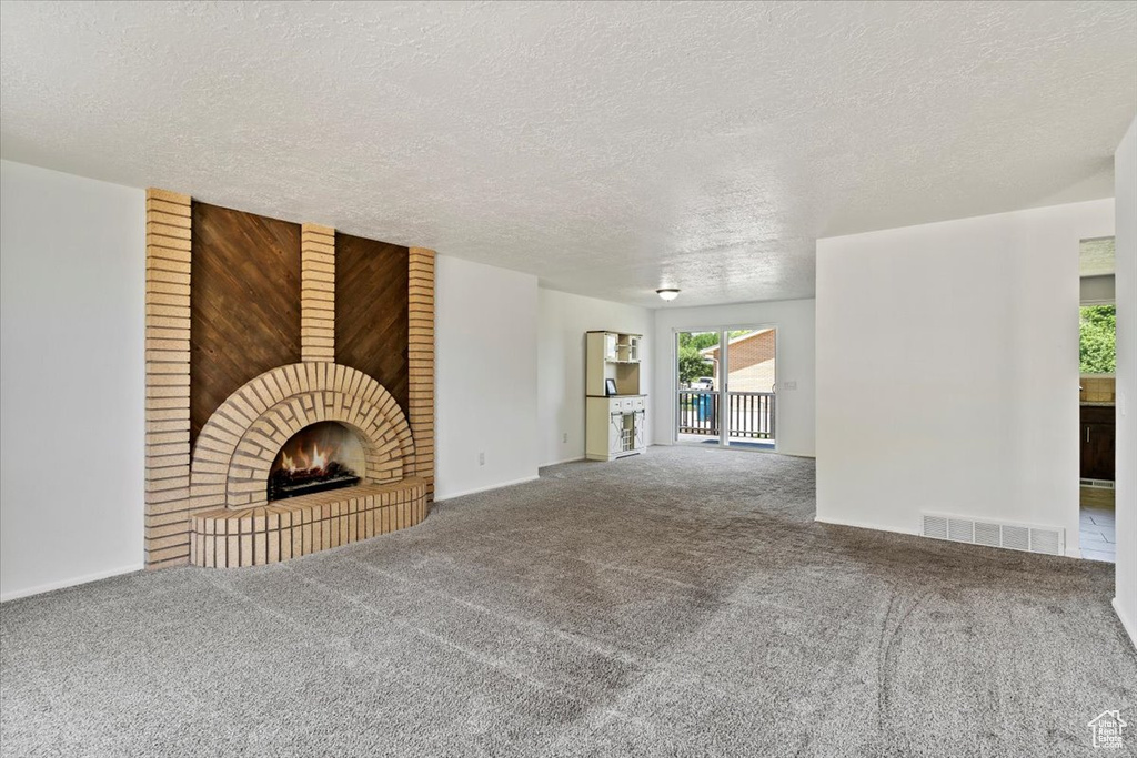 Unfurnished living room featuring a brick fireplace, carpet, and a textured ceiling