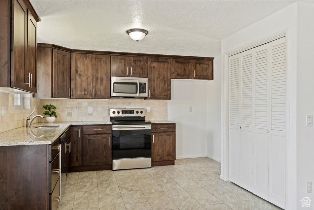 Kitchen with stainless steel appliances, tasteful backsplash, dark brown cabinets, light stone counters, and a textured ceiling