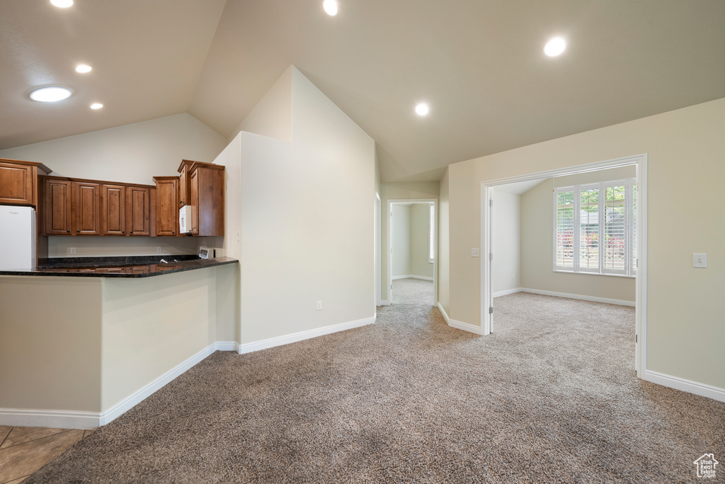 Kitchen with lofted ceiling, light colored carpet, recessed lighting, brown cabinets, and white microwave