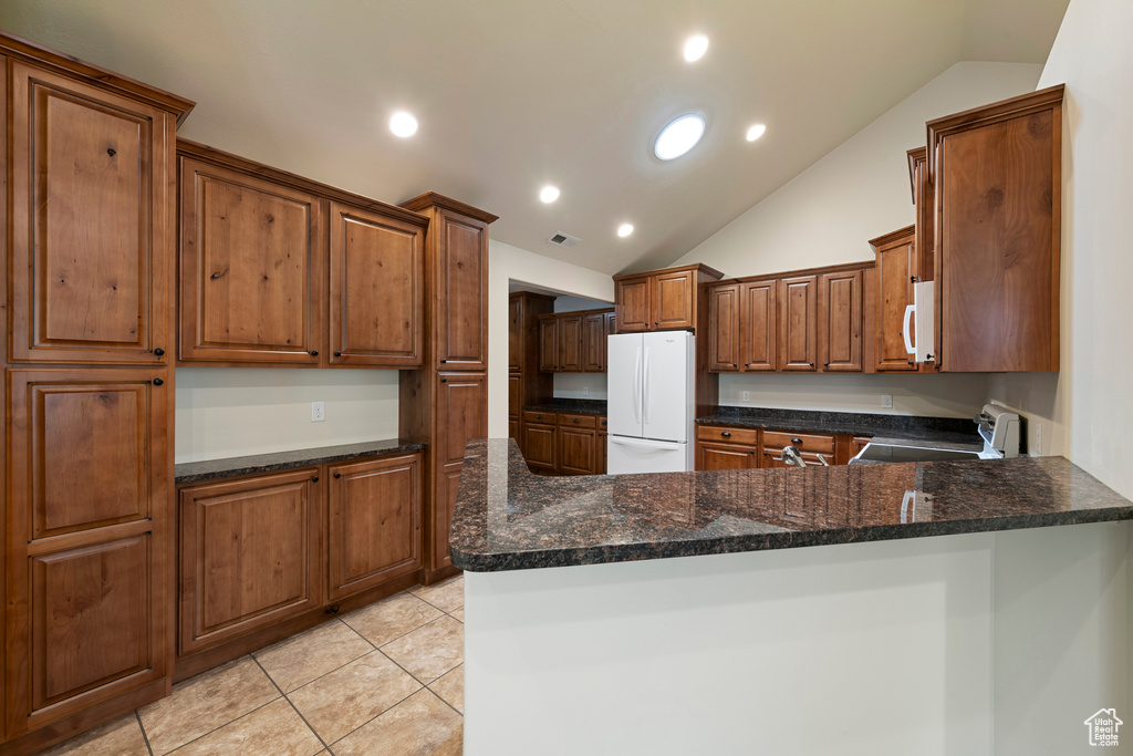 Kitchen featuring white appliances, vaulted ceiling, a peninsula, light tile patterned floors, and brown cabinets