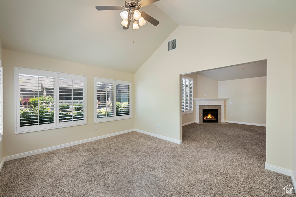 Unfurnished living room with carpet floors, high vaulted ceiling, ceiling fan, and a tiled fireplace