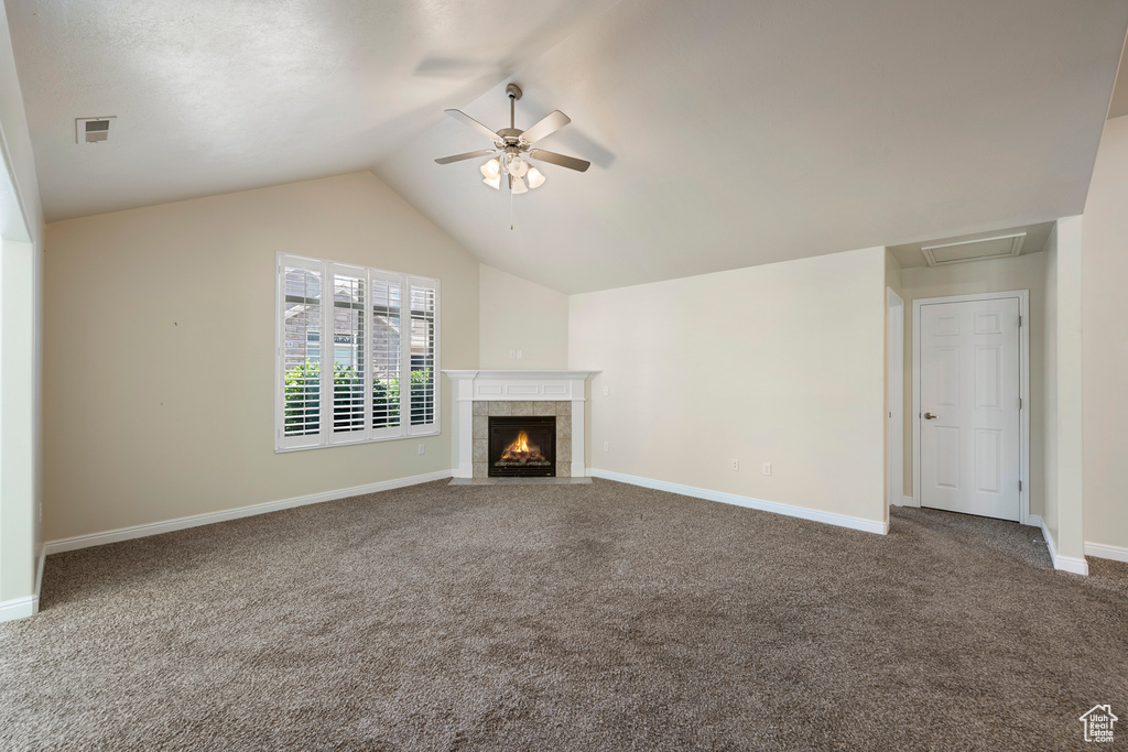 Unfurnished living room featuring carpet floors, a ceiling fan, vaulted ceiling, and a tiled fireplace