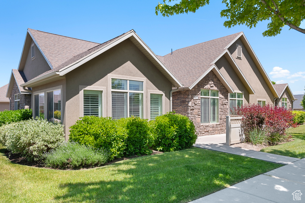 View of front of property featuring stone siding, stucco siding, a front lawn, and a shingled roof