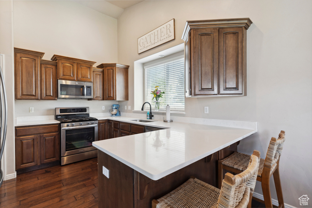 Kitchen featuring appliances with stainless steel finishes, a peninsula, a kitchen bar, dark wood-style floors, and light countertops