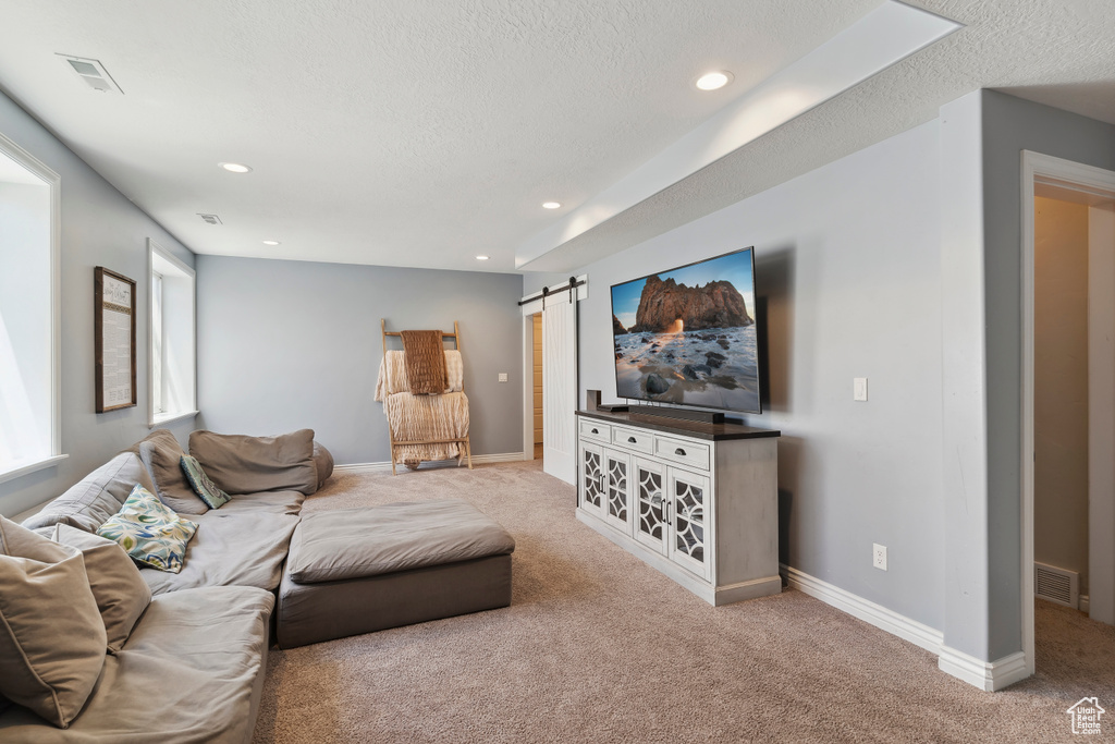 Living area with carpet flooring, a barn door, a textured ceiling, and recessed lighting