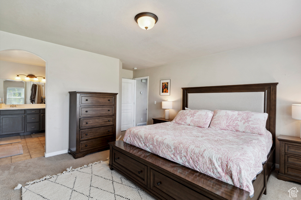 Bedroom with light carpet, arched walkways, and ensuite bath