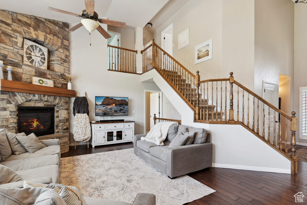 Living area featuring a high ceiling, dark wood finished floors, ceiling fan, stairs, and a stone fireplace