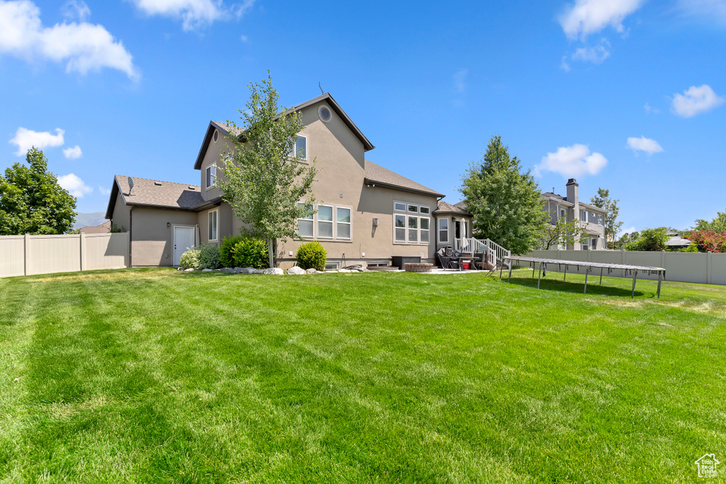 Rear view of property featuring a trampoline, a fenced backyard, and stucco siding