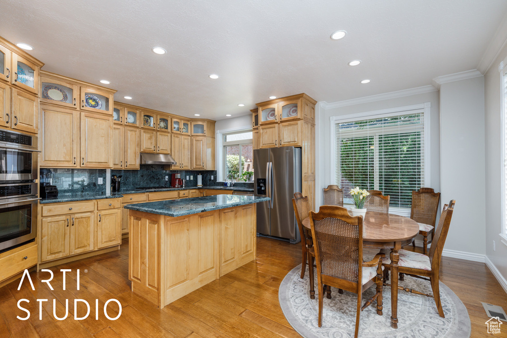 Kitchen with appliances with stainless steel finishes, under cabinet range hood, ornamental molding, a center island, and decorative backsplash