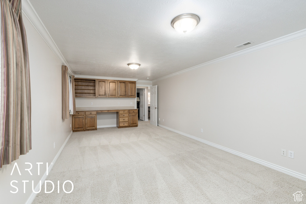Unfurnished living room with built in desk, ornamental molding, and light colored carpet