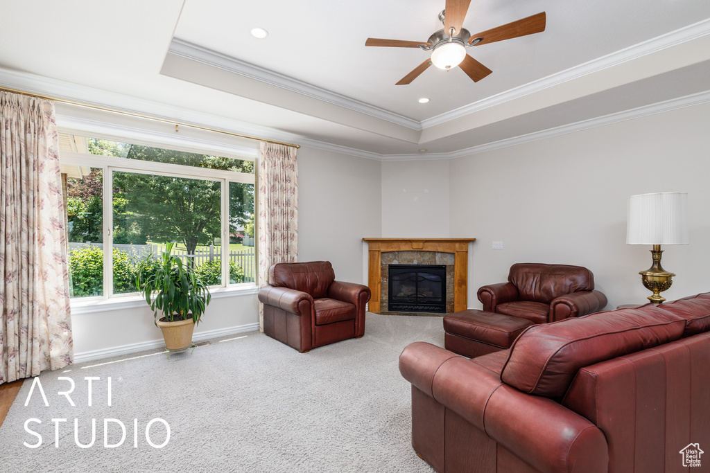 Living area featuring a raised ceiling, ornamental molding, a ceiling fan, a tiled fireplace, and carpet flooring