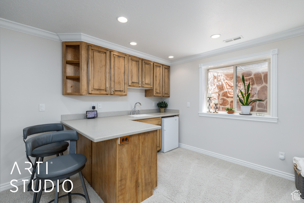 Kitchen featuring dishwashing machine, a kitchen breakfast bar, brown cabinets, light countertops, and light colored carpet