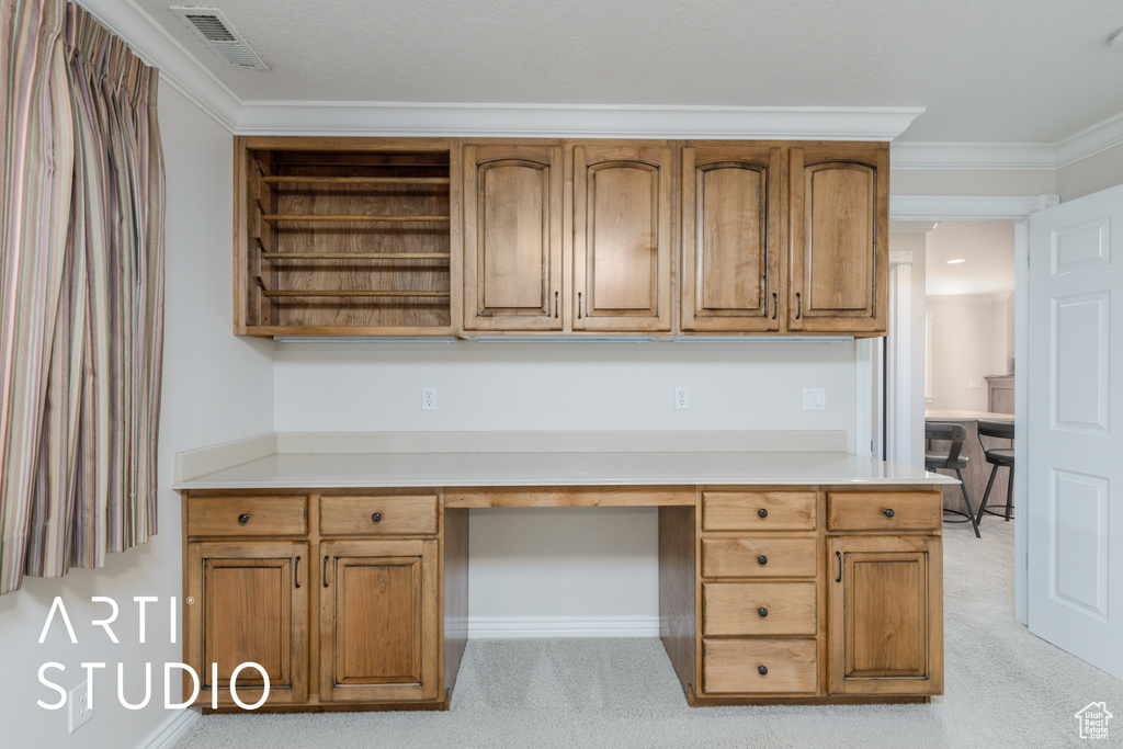 Unfurnished office featuring built in desk, light carpet, and crown molding