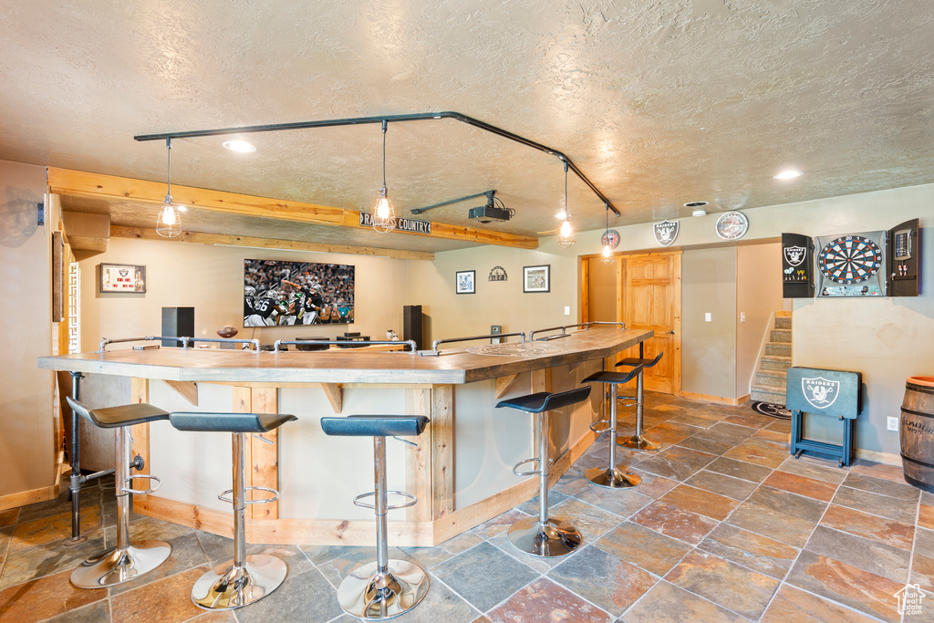 Indoor wet bar with a textured ceiling, stone tile floors, stairs, decorative light fixtures, and recessed lighting