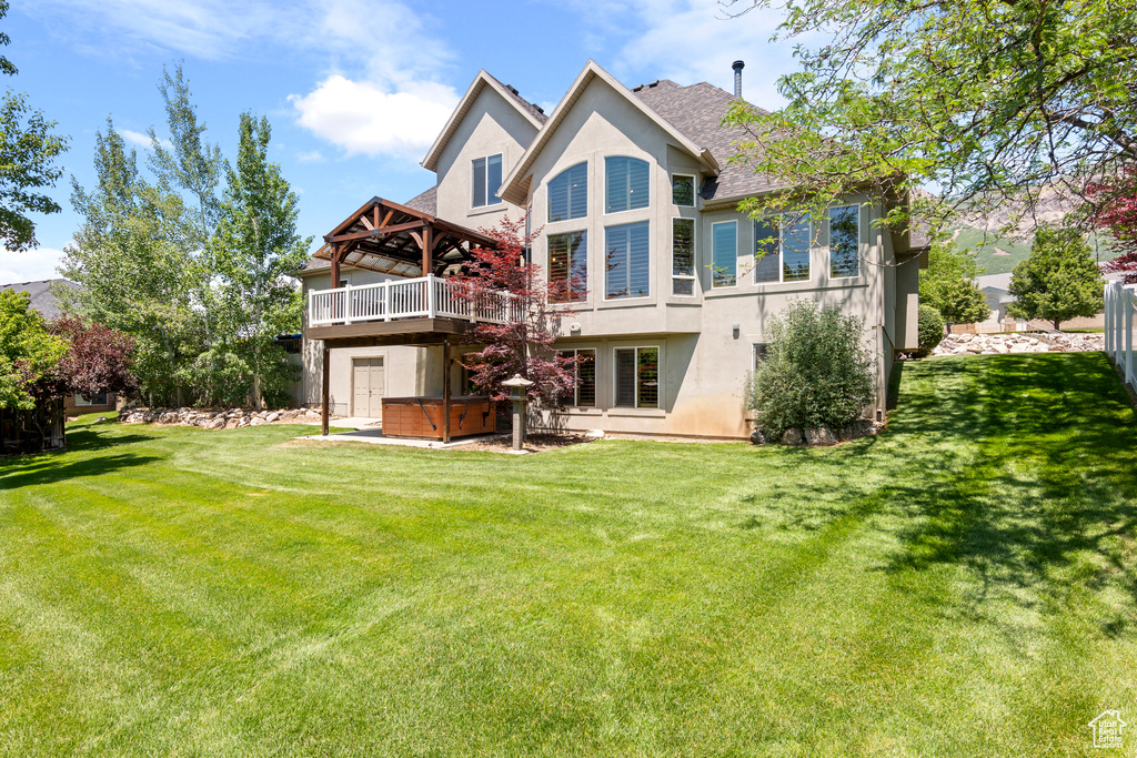 Back of property featuring a hot tub, stucco siding, a lawn, and a wooden deck