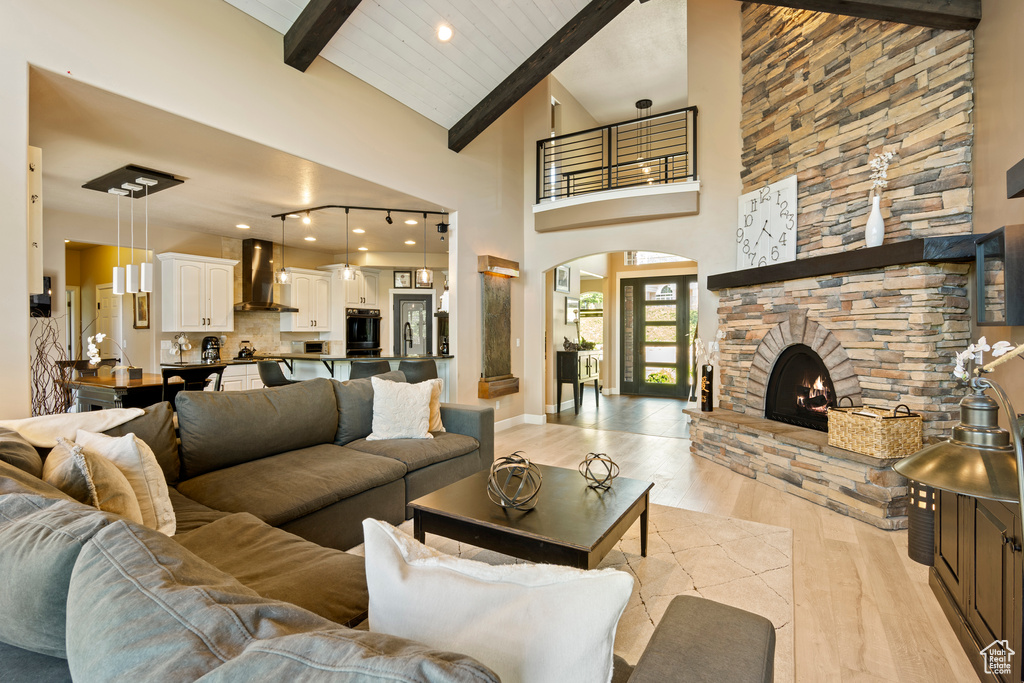 Living room with light wood-style flooring, beam ceiling, arched walkways, a fireplace, and high vaulted ceiling