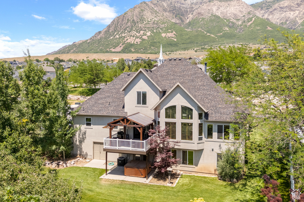 Back of house featuring stucco siding, a hot tub, a shingled roof, a patio, and a deck with mountain view