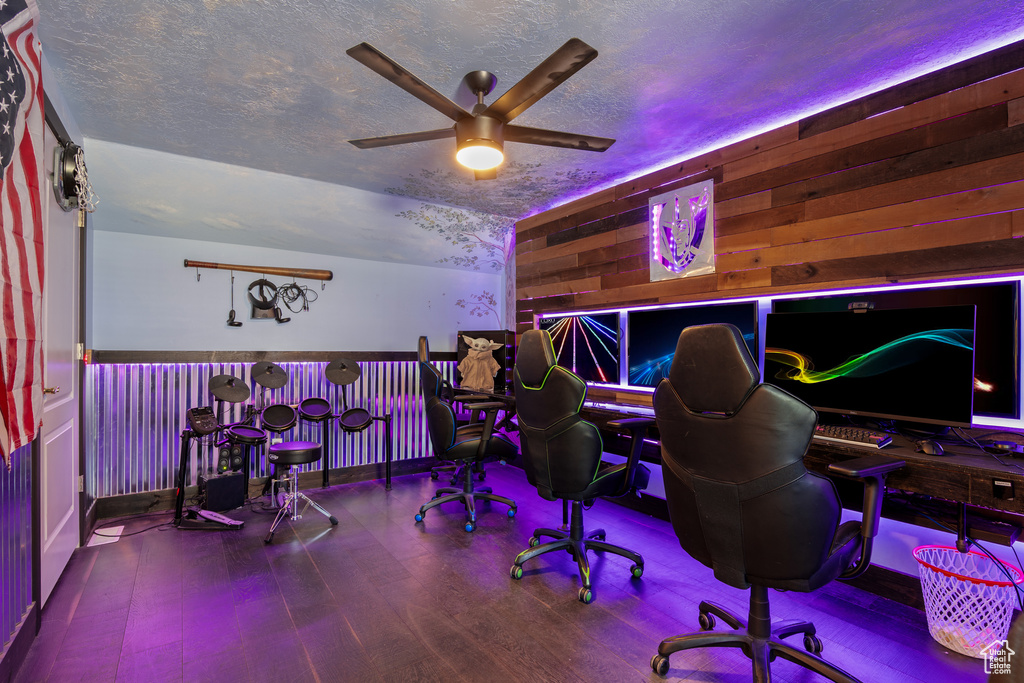 Home office featuring a ceiling fan, wood finished floors, a textured ceiling, and wooden walls