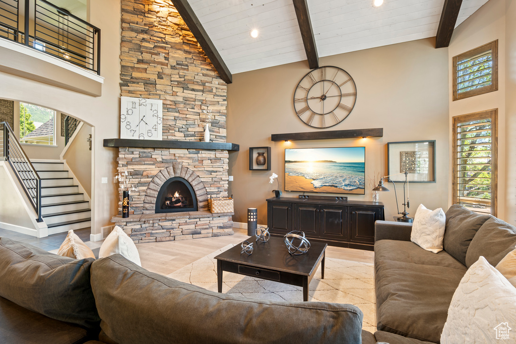 Living room featuring high vaulted ceiling, stairs, beamed ceiling, a stone fireplace, and recessed lighting