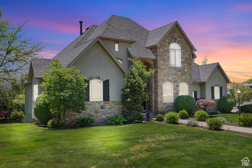 French country style house featuring stone siding, stucco siding, a lawn, and roof with shingles