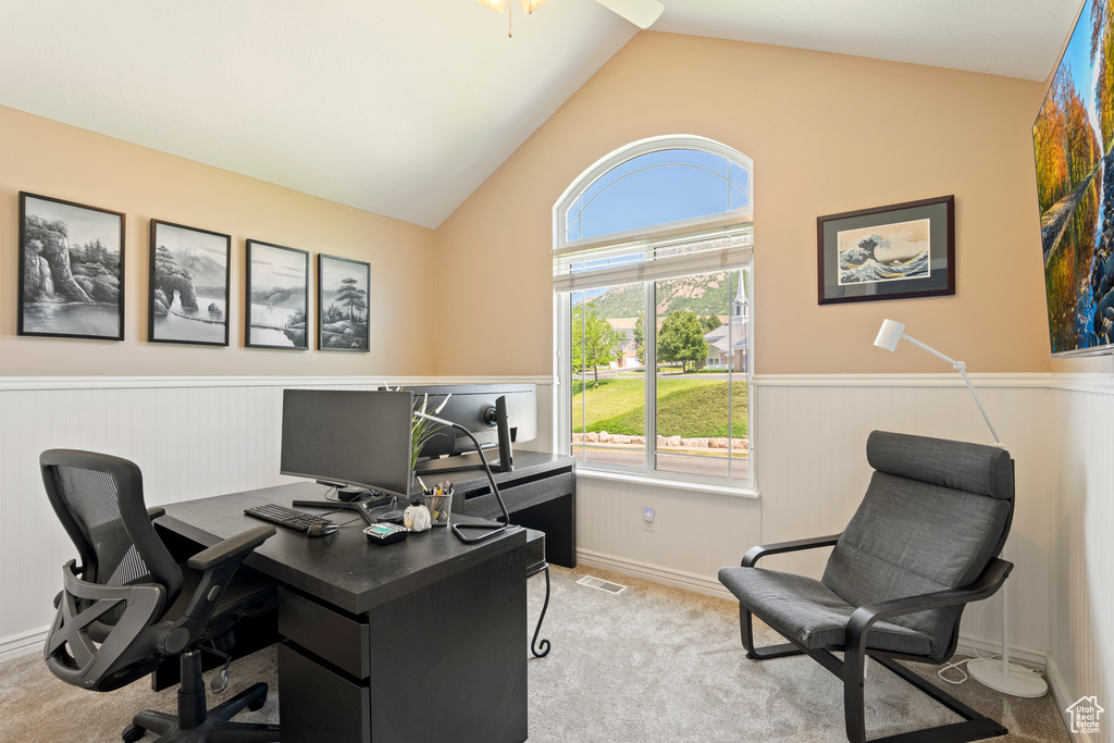 Carpeted home office with a wainscoted wall and lofted ceiling