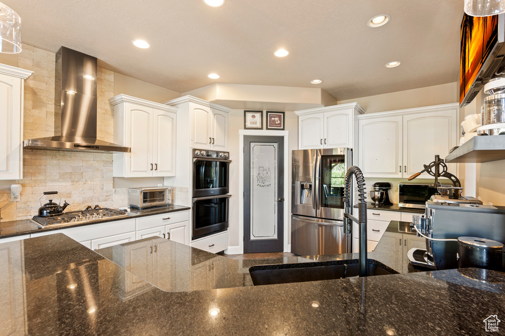 Kitchen with wall chimney range hood, appliances with stainless steel finishes, white cabinets, backsplash, and recessed lighting