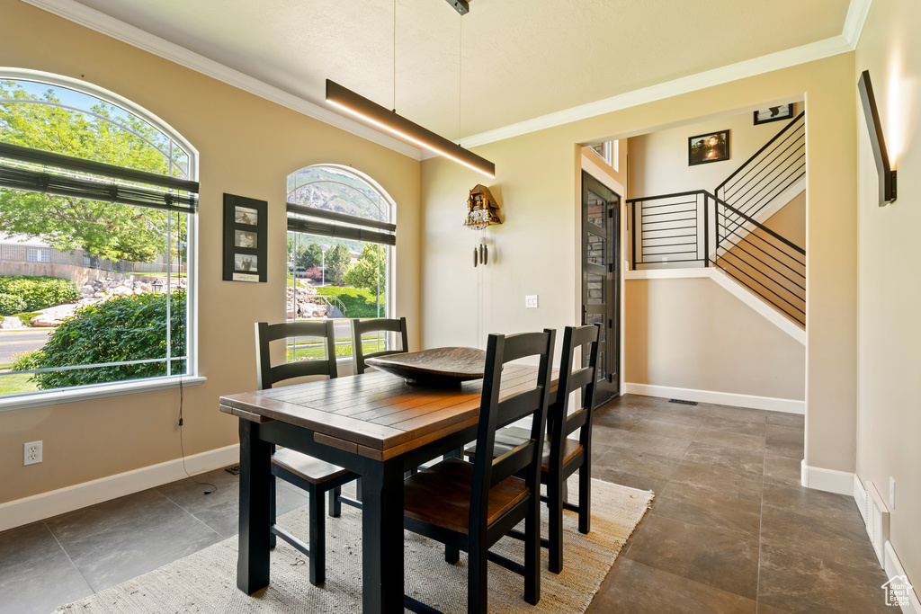 Dining area with ornamental molding, stairs, and dark stone finish floors