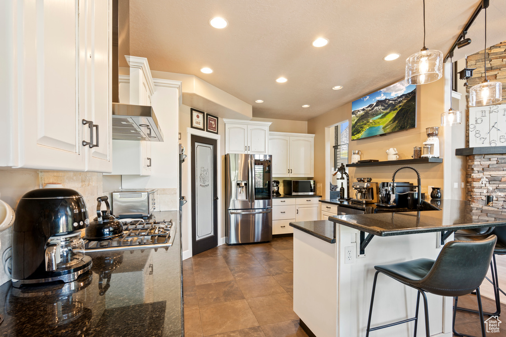Kitchen with appliances with stainless steel finishes, a peninsula, recessed lighting, white cabinetry, and wall chimney range hood