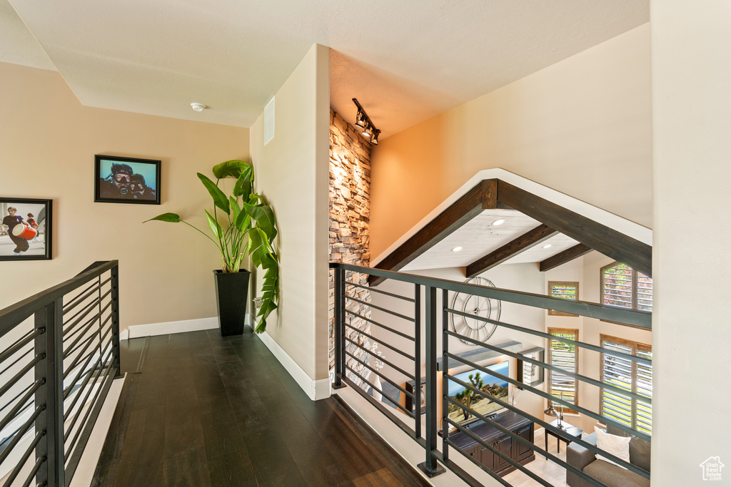 Hallway with an upstairs landing, wood finished floors, and beam ceiling