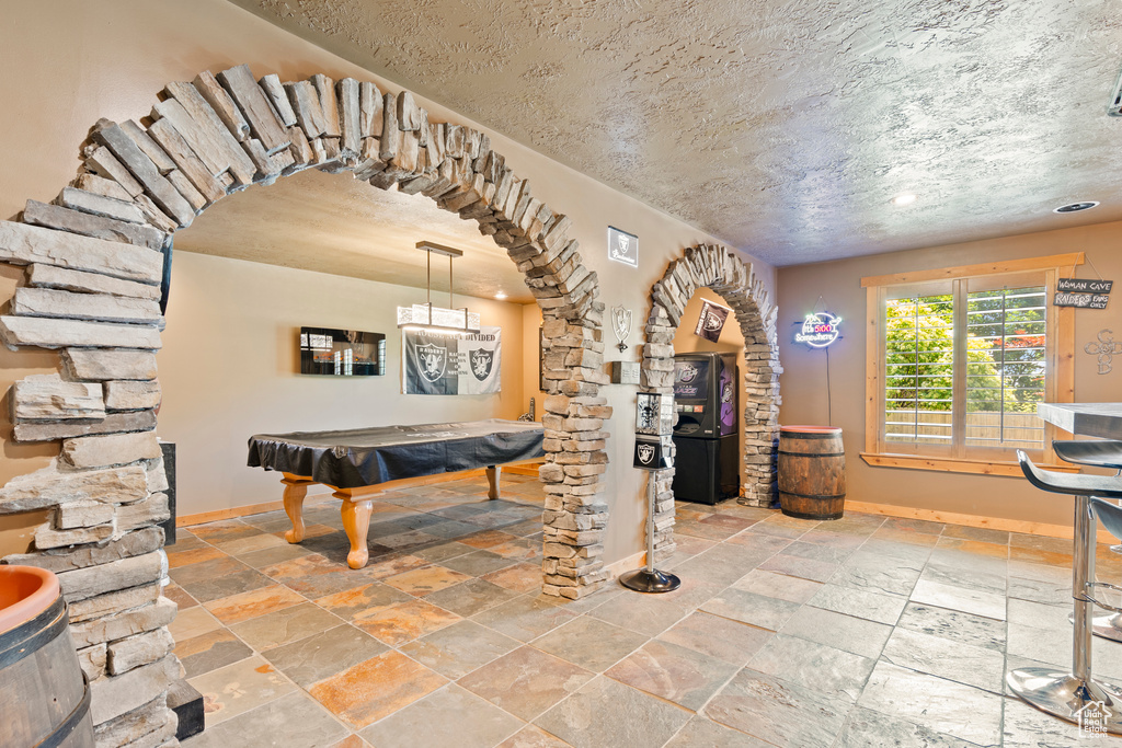 Rec room with billiards table, stone tile floors, arched walkways, and a textured ceiling