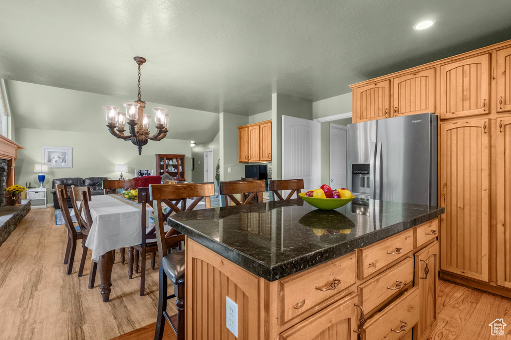 Kitchen featuring stainless steel fridge with ice dispenser, a chandelier, light wood finished floors, a kitchen bar, and pendant lighting