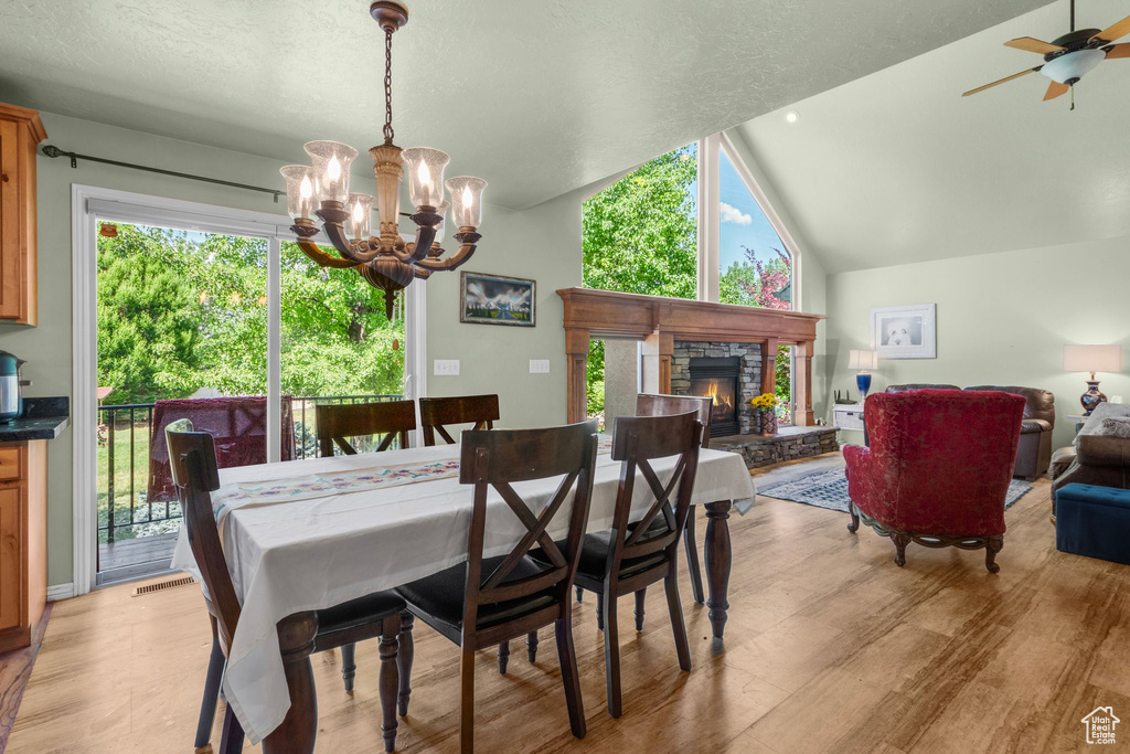 Dining area with a chandelier, a fireplace, lofted ceiling, light wood finished floors, and ceiling fan