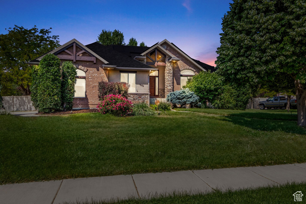 View of front of property with a front yard, stone siding, and roof with shingles