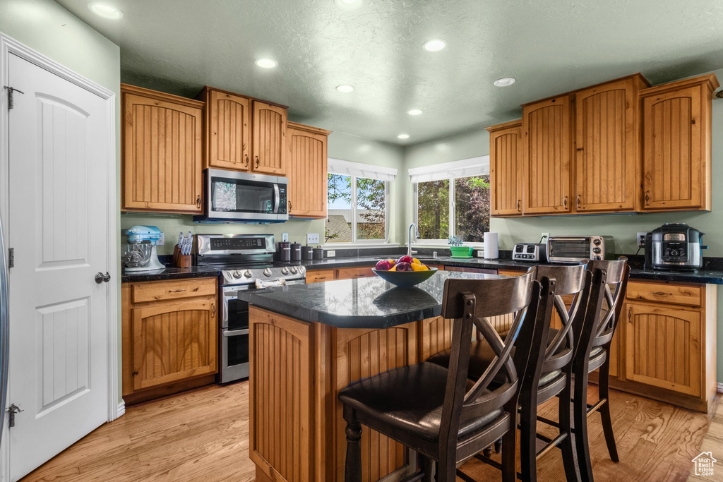 Kitchen featuring appliances with stainless steel finishes, recessed lighting, a kitchen island, a breakfast bar, and light wood finished floors