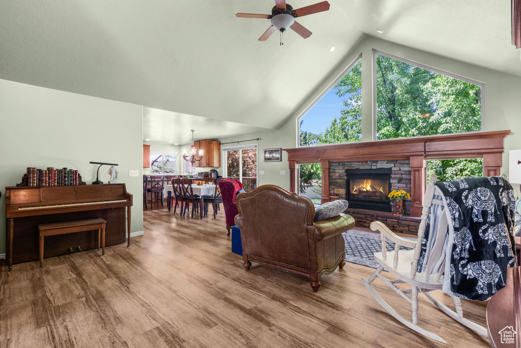 Living area with ceiling fan, wood finished floors, a chandelier, high vaulted ceiling, and a fireplace