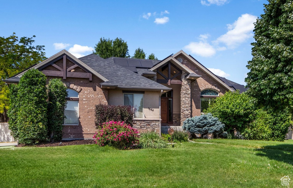 View of front of house with a shingled roof, a front yard, stone siding, stucco siding, and brick siding