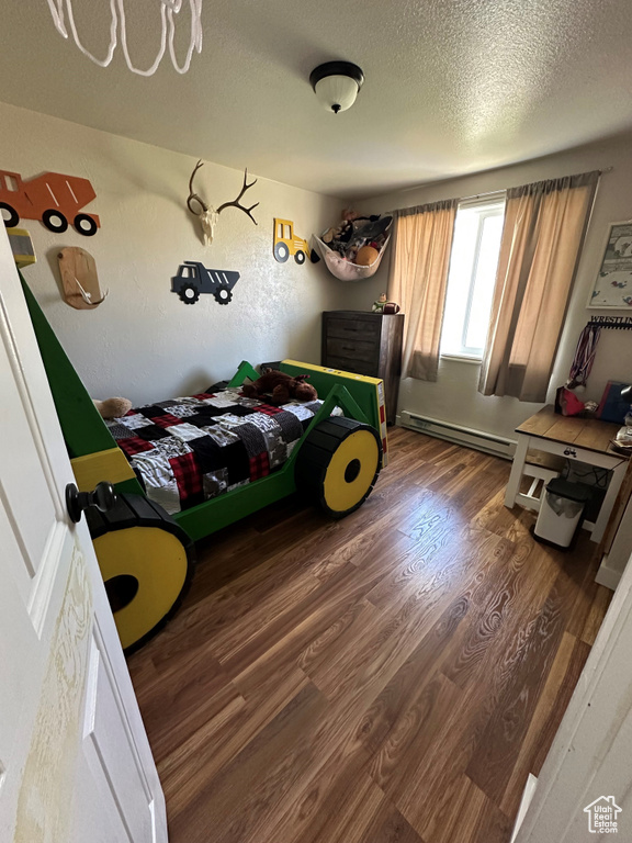 Bedroom featuring a baseboard heating unit, wood finished floors, and a textured ceiling