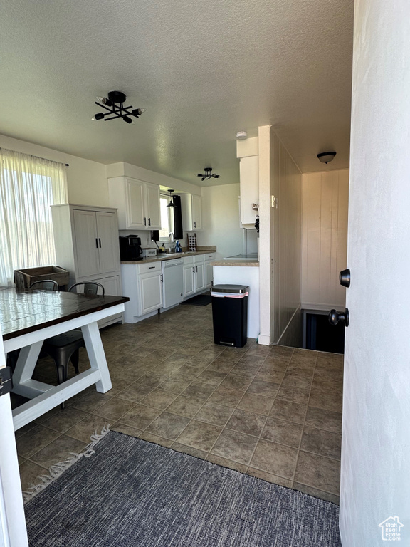 Kitchen with a textured ceiling, white cabinetry, white dishwasher, and dark tile patterned floors