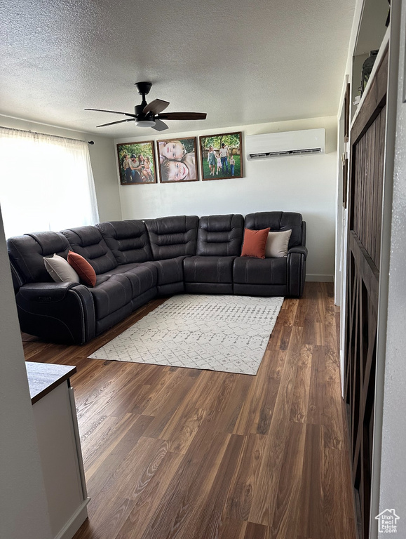 Living area featuring a wall mounted air conditioner, a ceiling fan, dark wood-type flooring, and a textured ceiling