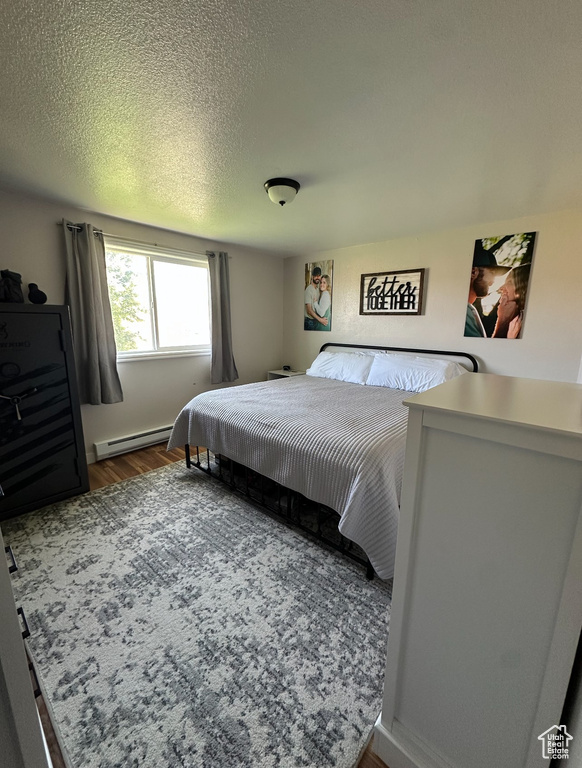 Bedroom with a baseboard heating unit and wood finished floors