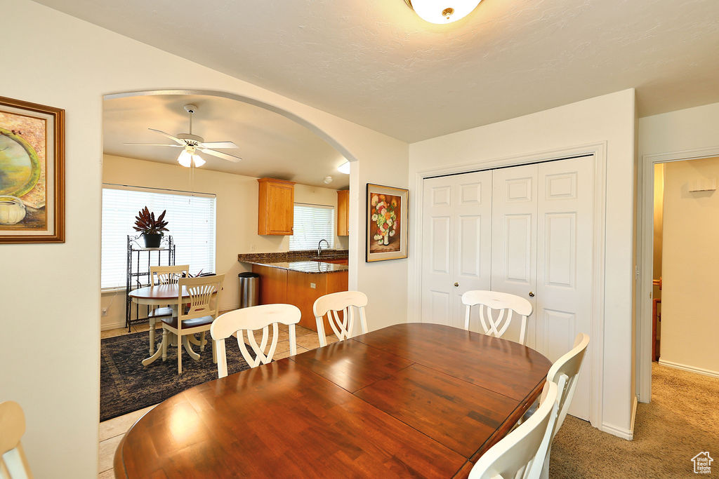 Dining space featuring arched walkways, a ceiling fan, and light carpet